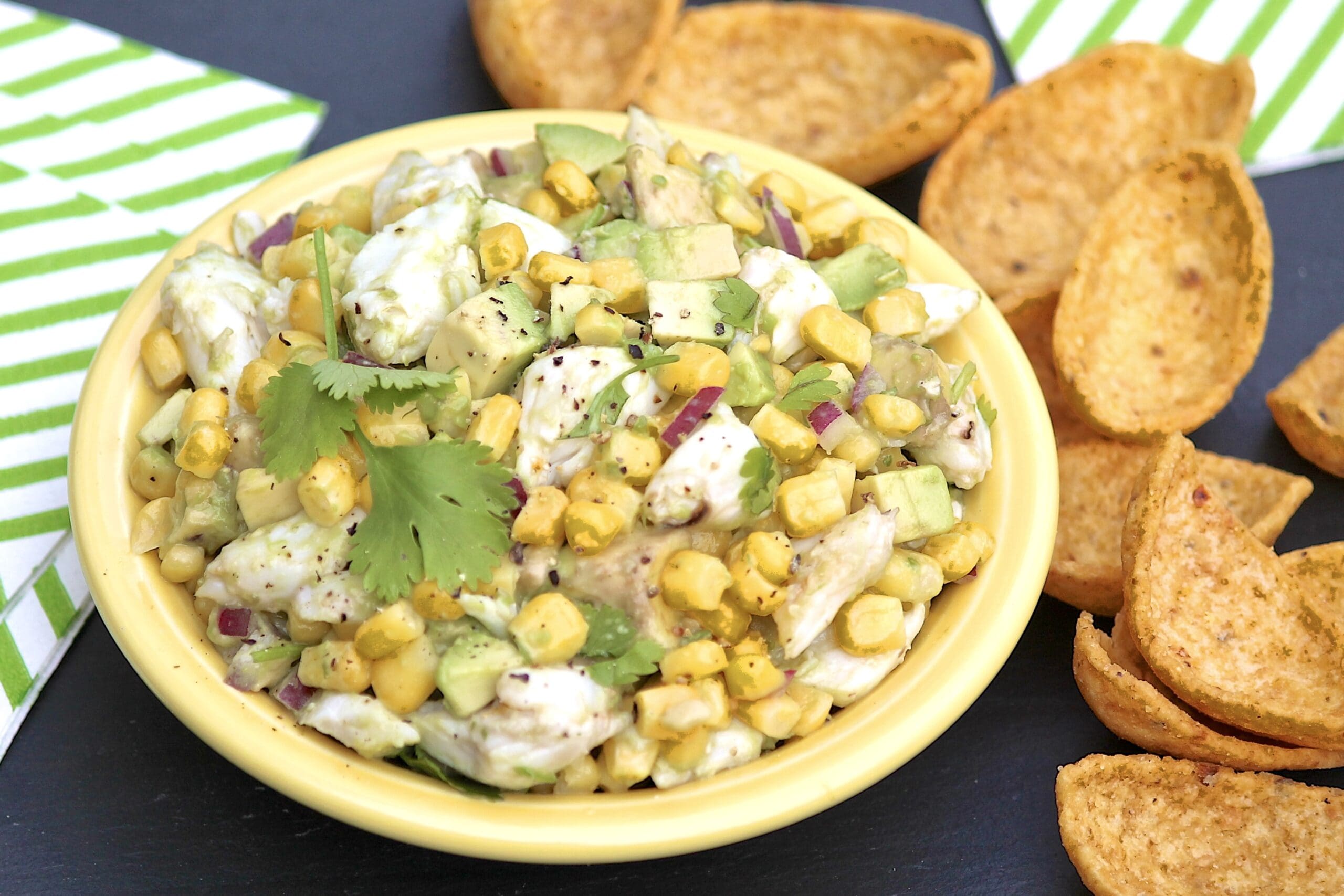 An overhead shot of a plated crab, avocado and charred-corn salad in a wide white bowl.